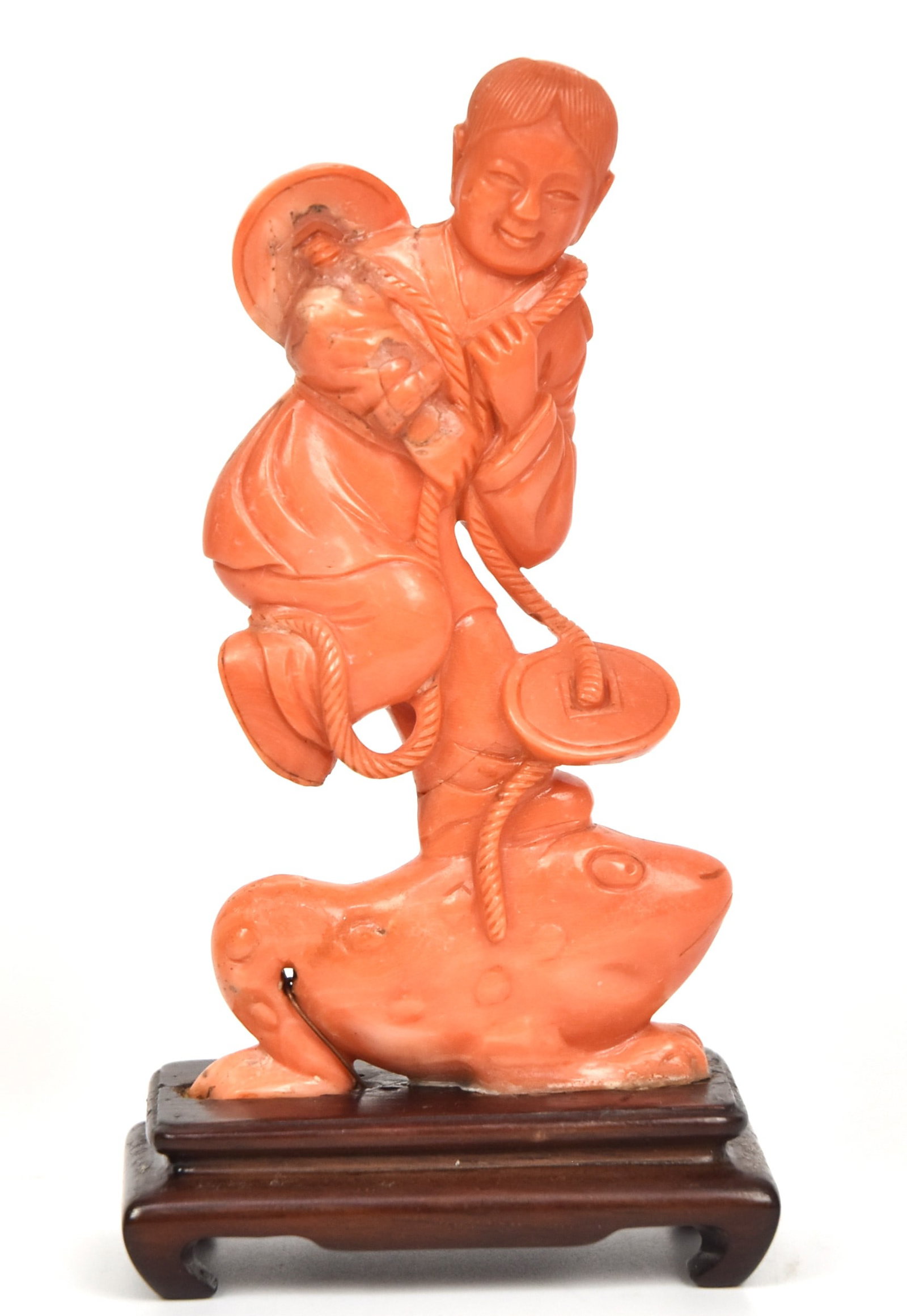 Chinese Orange Coral Carving: Figure of a youth standing atop a giant frog with net floats, mounted on teak stand, 4 3/4" high. Condition Fine.