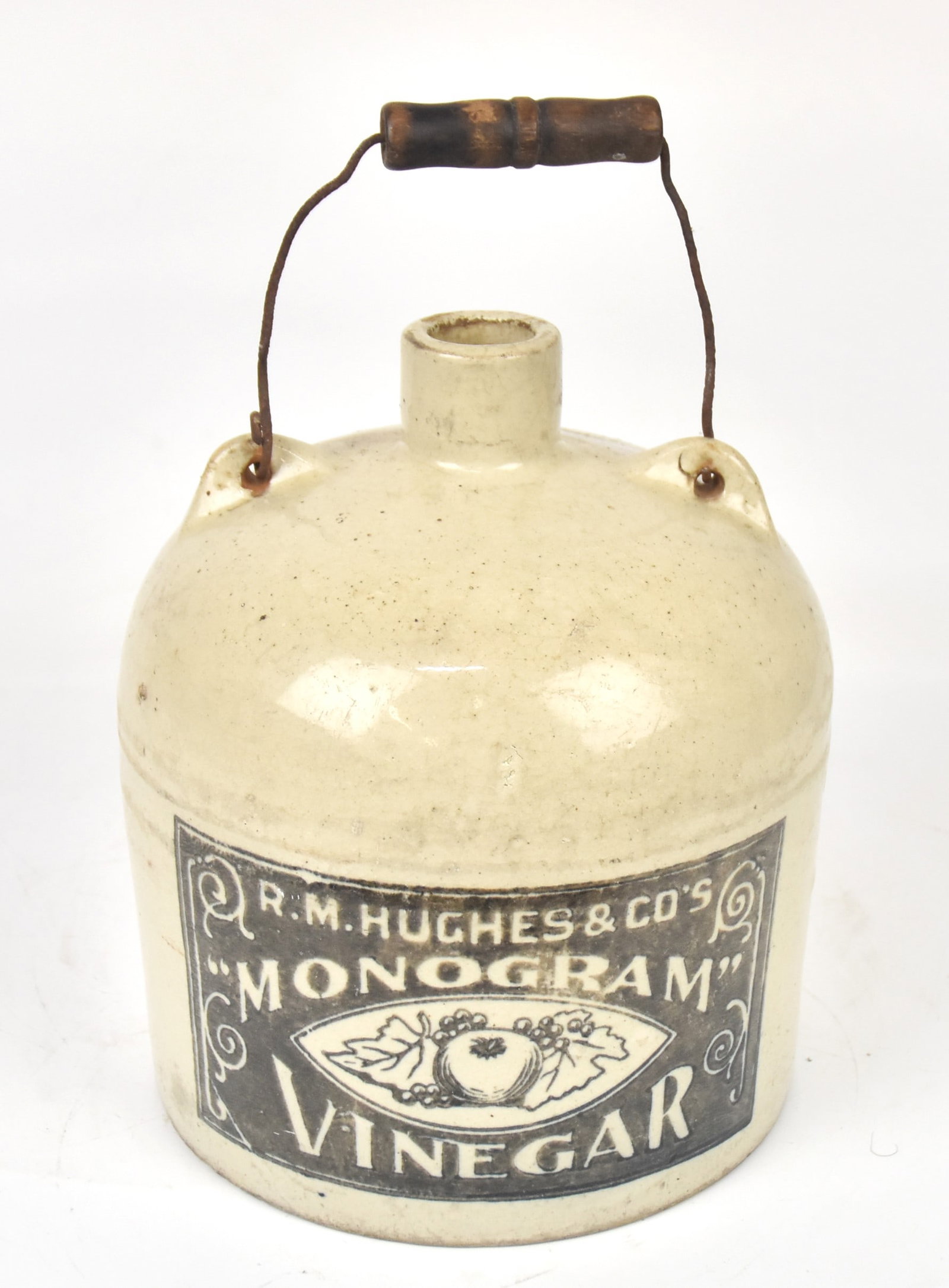 R.M. Hughes Vinegar Stoneware Jug: With wire and wood handle. 12" H x 7 1/4" Dia. Two minor glaz nicks to surface; otherwise good condition.