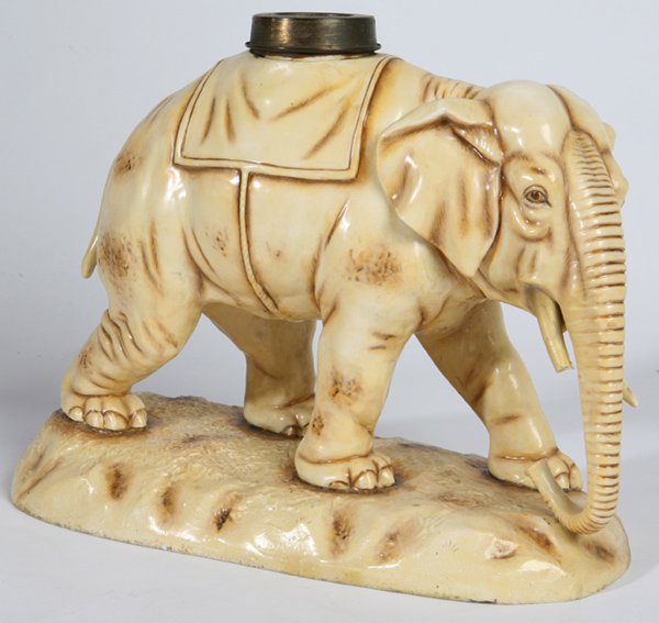 ROYAL DUX TYPE ELEPHANT OIL LAMP BASE: Porcelain in the form of a full figured African elephant with brass collar for font. Marked on base. One tusk broken. 13" long x 10 1/2" h.