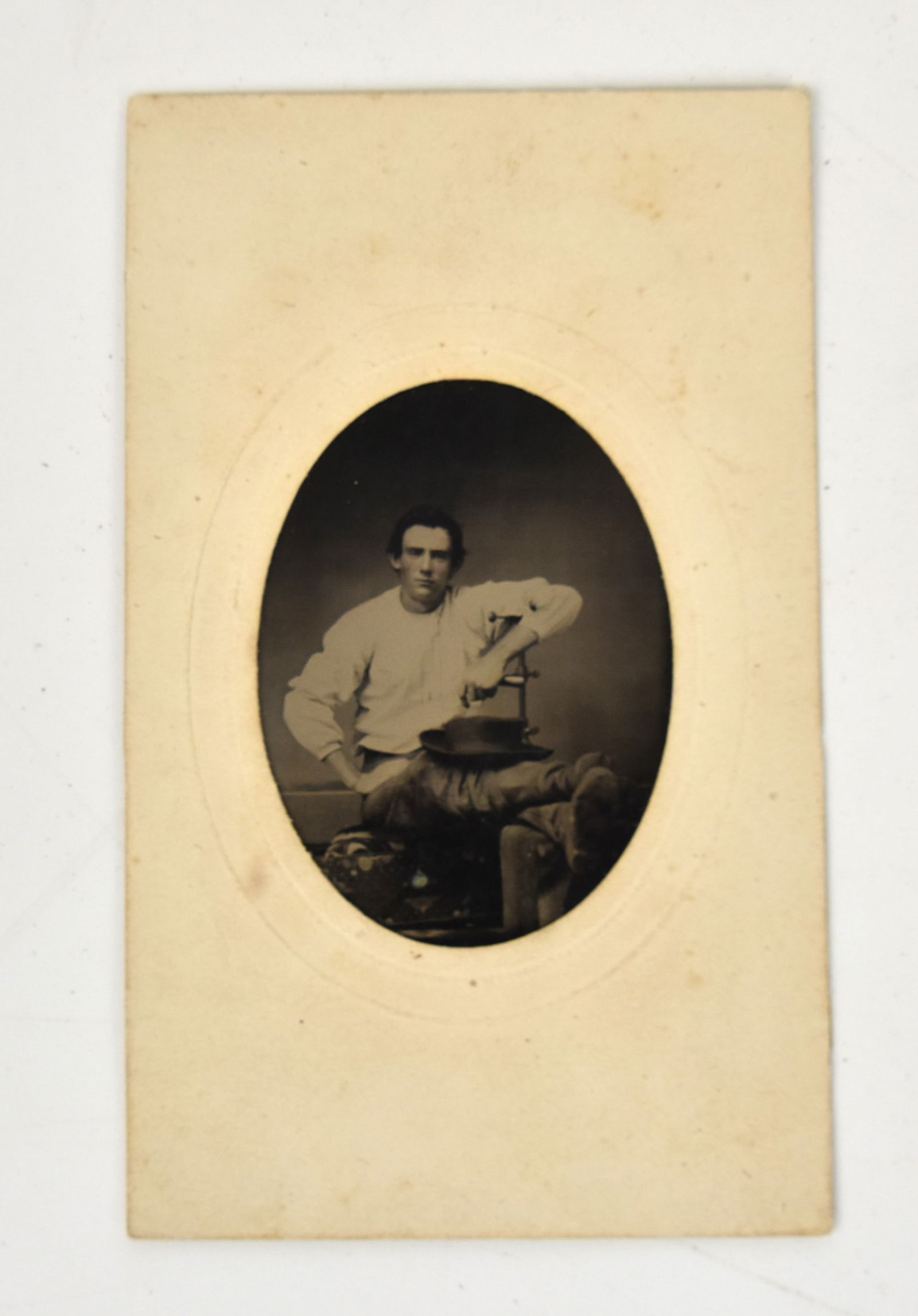 Civil War Tintype of Amputee Soldiers: CDV sized mounted in original paper sleeve showing a young man seated with both legs elevated with hardee style hat in lap, his left foot is missing. Condition VG.