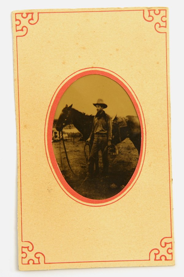CDV TINTYPE PHOTO OF COWBOY W/HORSE: Anonymous cdv sized image in printed paper mount of a young cowboy with broad brimmed hat and lasso, saddled horse behind.