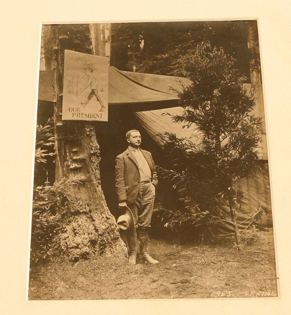 BOHEMIAN GROVE PHOTO BY MOULIN: A Moulin Studio photograph showing a young gentleman (Wm. H. Irwin) in hunting boots with park ranger type hat in hand standing next to a tree with a hand drawn caricature of himself with the text “