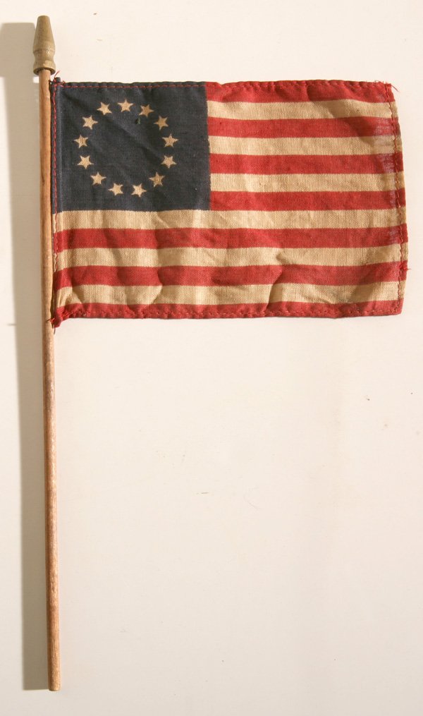 13 STAR U.S. CENTENNIAL PARADE FLAG: In printed linen with canton having ring of 13 stars, machine sewn edges and mounted on original shaft with gilt painted turned finial. Flag is 4 x 6”, shaft is 10.25.