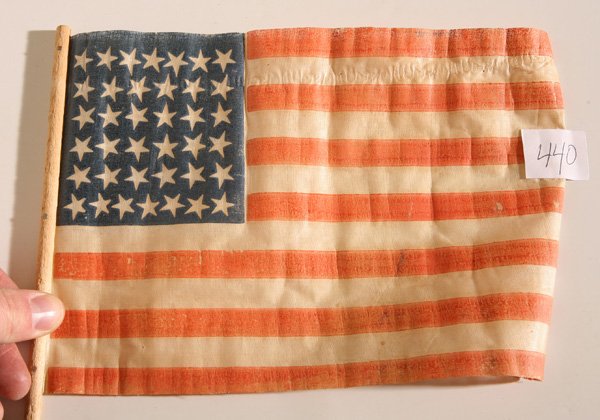 38 STAR U.S. CENTENNIAL PARADE FLAG: Printed linen and glazed with canton patter of 7-6-6-6-6-7, mounted on original turned wood stick, 7 x 10” with 18” stick.