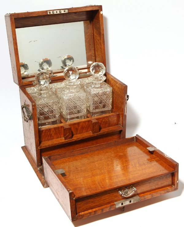 Fine Edwardian Tantalus: In oak with three cut glass decanters with original stoppers, mirrored back and lid with shelves for three decks of playing cards, divided drawer for poker chips, nickel plated brass tabs to hold pape
