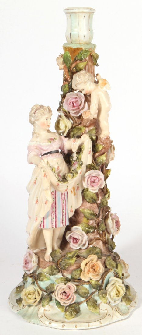 Sitzendorf Porcelain Figural Candlestick: With full figure of a young maiden holding her skirt up while Cupid drops flowers into it, picked from tree form stem, covered in roses, all hand painted with blue underglaze crossed lines marks, 6.5"
