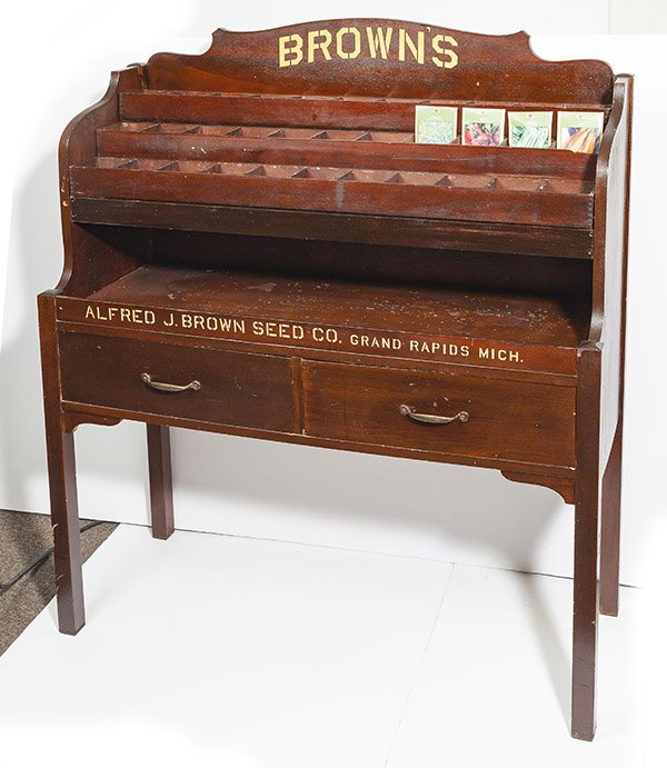 Bown Seed Display Cabinet: in mahogany with original varnish finish and handles with three stepped, divided, & removable shelves at top over two dovetailed drawers, scroll cut crest with gold "Brown" over "Alfred J. Brown Seed 