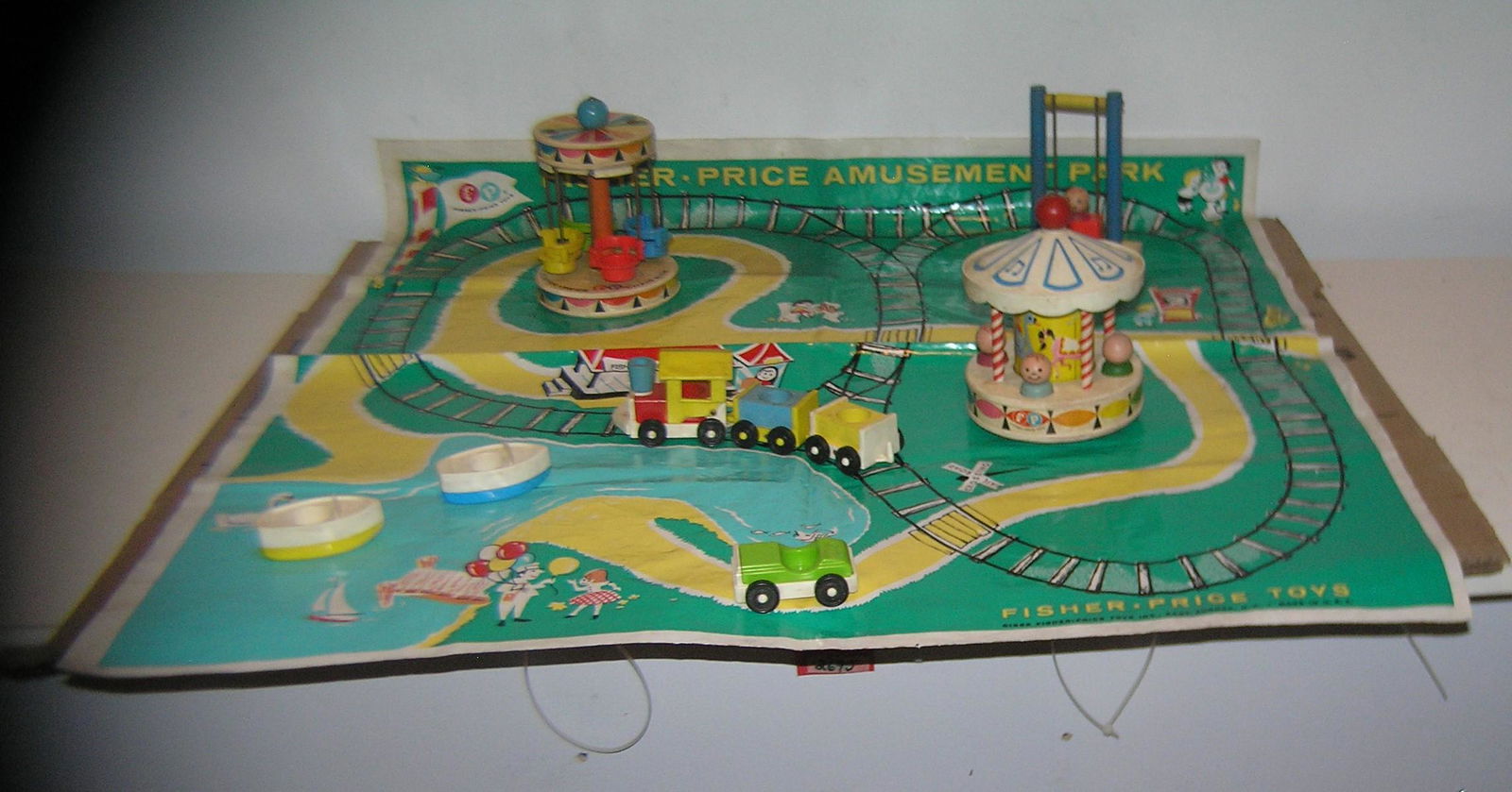 Early Fisher Price amusement park play set: Early Fisher Price amusement park play set dated 1963 includes Theme park place mat, Merry Go Round, chair ride, swing, train set, automobile and boat est. Value $175.00-$200.00