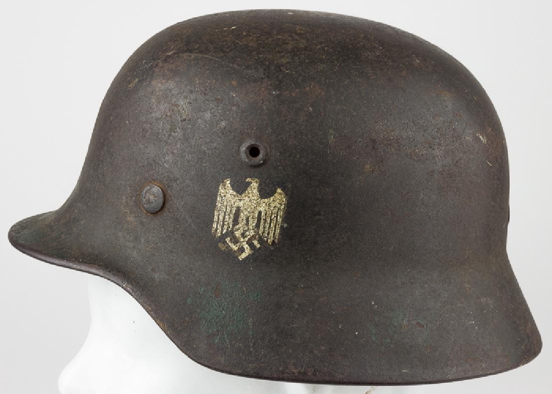 GERMAN HEER M1940 COMBAT HELMET: GERMAN HEER M1940 COMBAT HELMET German Heer M1940 helmet with single eagle and swastika decal affixed at left, painted in a very light gray-black textured paint, though there are a few very small area