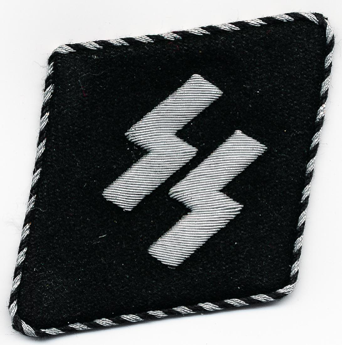 DUTCH SS SLEEVE RAUTE: DUTCH SS SLEEVE RAUTE Black felt diamond-shaped sleeve insignia, 2 1/2" x 3", depicting the SS "sig" runes in silver metal thread, with silver and black piping. A paper RZM tag is present on the rever