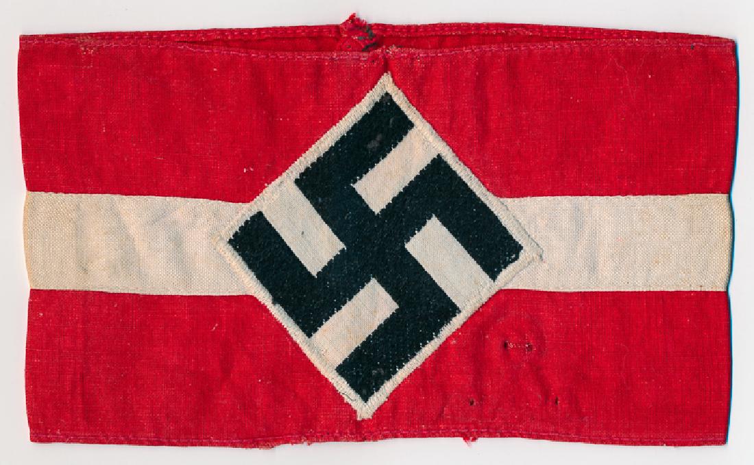 HITLER YOUTH ARMBAND: HITLER YOUTH ARMBAND Red cotton armband, 7" x 4", bearing a white applied band, with an embroidered mobile swastika in the center. Lightly soiled, with four pinholes to the left of the insignia, else 