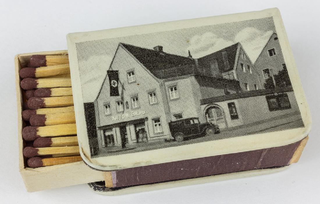 MATCHBOX COVER WITH NSDAP FLAG: MATCHBOX COVER WITH NSDAP FLAG Enameled metal matchbox cover, 2 1/4" x 1 1/2" x 1/2", advertising the tobacconist Anton Brau of Pfaffenburg, featuring a b/w image of the shop, which proudly flies an N