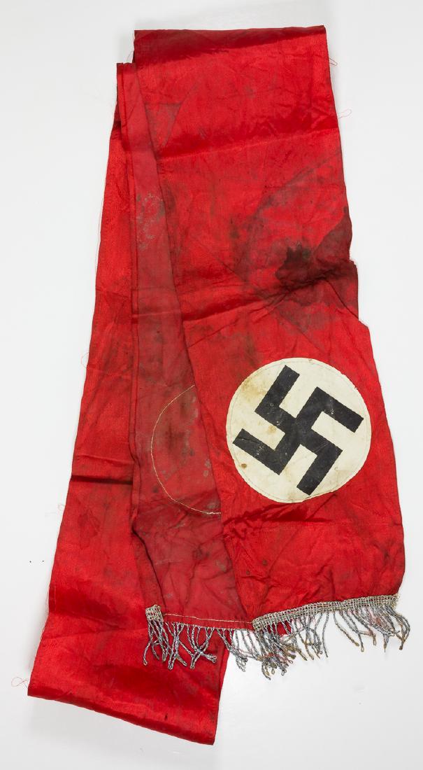 NSDAP FUNERAL SASH: NSDAP FUNERAL SASH Red rayon banner, 77" x 5 1/4", with a white paper disk with a printed mobile swastika at each end. Each end also features a 1 1/2" silver metallic fringe. The sash is stained throu