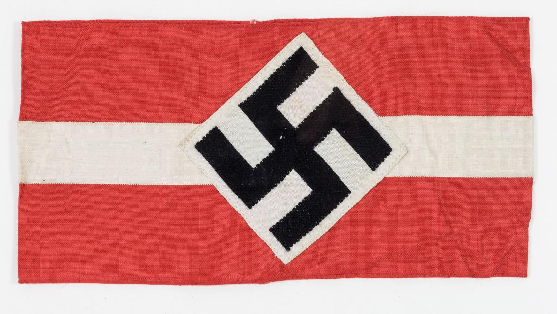 HITLER YOUTH ARMBAND: Red cotton armband, 7" x 4", bearing a white applied band, with an embroidered mobile swastika on a white cloth diamond at center. In fine condition.
