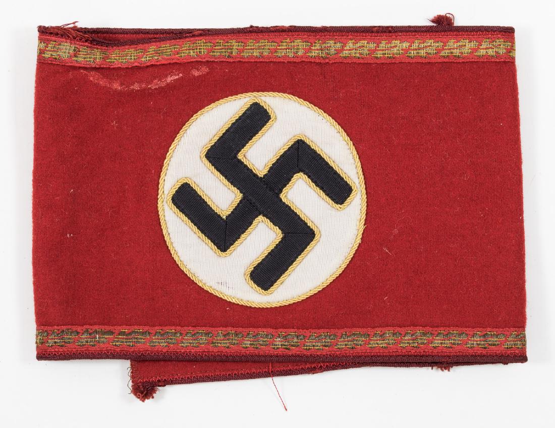 NSDAP GAU-LEVEL ARMBAND: Red wool gau-level party leader's armband, 5" x 20" unfolded, with a 3 1/4" dia. white fabric disc machine-sewn with a hand-sewn braided gold thread border at center, bearing a black ribbon swastika,