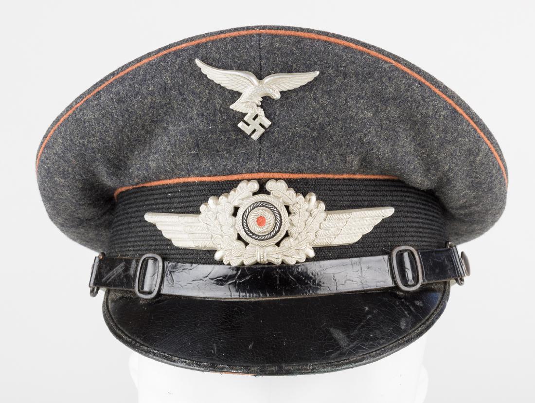 LUFTWAFFE SIGNALS VISOR CAP BY CLEMENS WAGNER: Fine example of a visor cap as worn by an non-commissioned officer of the Luftwaffe Signals Corps, constructed of blue-grey wool with orange-brown piping encircling the crown and bordering the black m