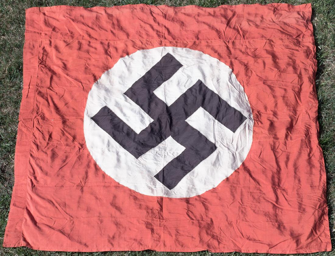 CAPTURED NSDAP BANNER: Large NSDAP hanging banner, 73" x 67", constructed of three sections of red rayon with a sewn-in white disk and mobile swastika at center. The hoist has been folded and sewn to form a pocket for a han