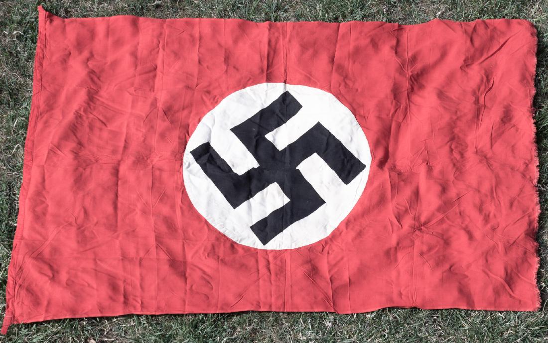 NSDAP FLAG: Large NSDAP flag, 69" x 44", of red cotton bunting with a sewn-on white disk on each side clamp-dyed with a black mobile swastika. The hoist is reinforced with an added strip of fabric, with cloth han