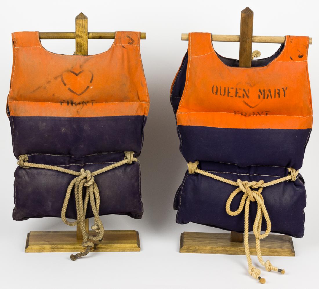 TROOP SHIP "QUEEN MARY" LIFE VESTS: Pair of original World War II-era life vests taken from the most notable troop transport of the conflict, the ocean liner R.M.S. QUEEN MARY. The first vest, approx. 44" x 14 Â½" fully opened, is con