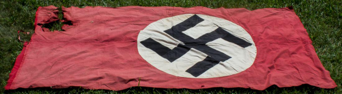 NSDAP FLAG: Larger Third Reich-era national flag, 112" x 56", two-piece double-sided red cotton bunting with a sewn-on white disk at center, clamp-dyed with a black mobile swastika. One end was folded over and se