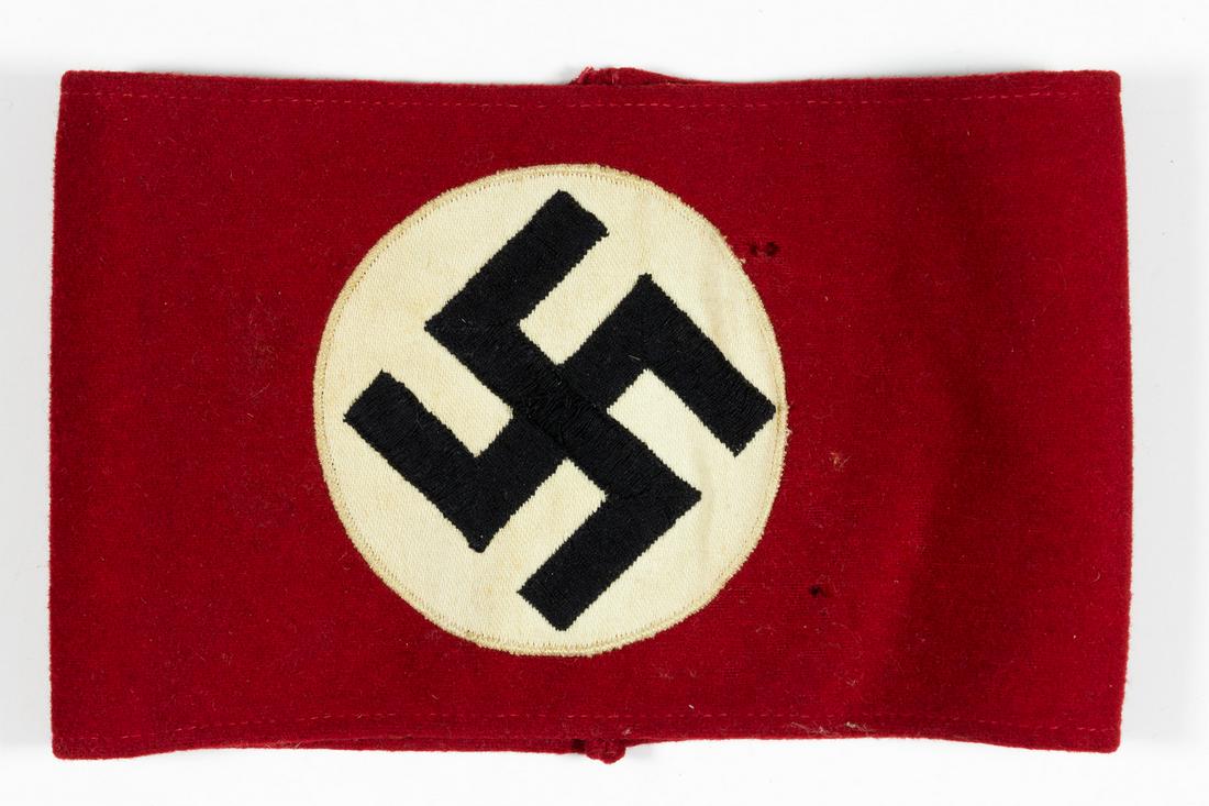 NSDAP ARMBAND: Red wool NSDAP armband, 7 3/4' x 4 3/4', with a white fabric disk at center enclosing an embroidered mobile swastika in black thread. Shows a few notable moth holes and smaller nips, else very good.