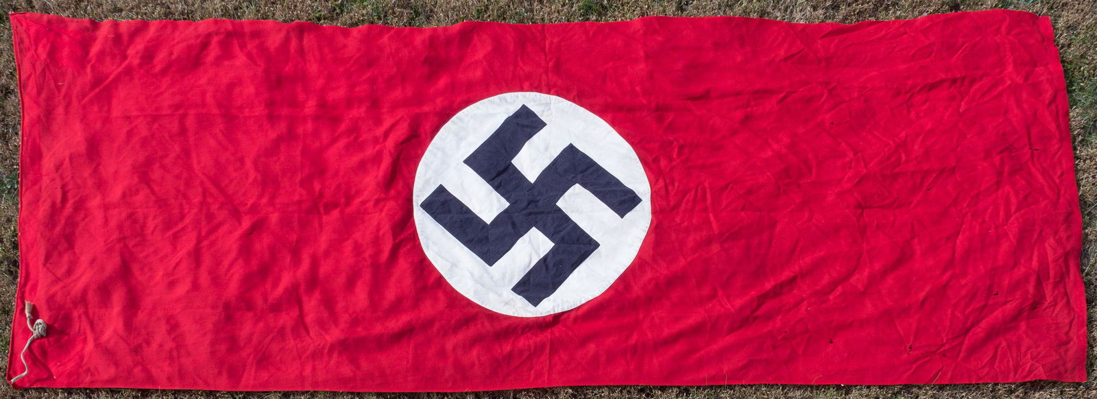 NSDAP FLAG "TAKEN FROM HITLER: Large NSDAP 'lager' or camp-style flag, 124 1/2' x 46', constructed of red wool bunting and bearing a sewn-on white cotton bunting disk, which in turn features a sewn-on black swastika. One edge is fo