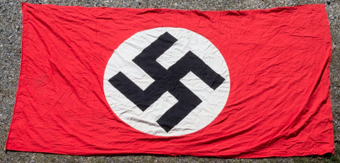 NSDAP FLAG: Large NSDAP flag, approx. 65 x 110 in., with both sides bearing a three-piece white disk sewn-on at center, each enclosing a sewn-on mobile swastika. The fabric is folded over and sewn on one end to f