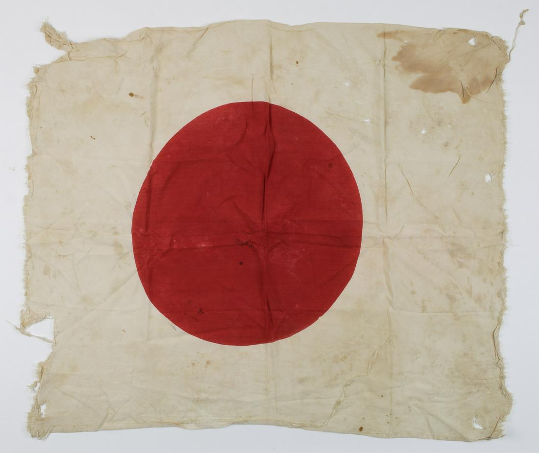 BLOOD-STAINED, BATTLE-DAMAGED JAPANESE NATIONAL FLAG: Japanese national flag 32 x 27.5 in. cotton clamp-dyed with a red "hinomaru" sun symbol at center. The itemâ€™s numerous tears and ragged edges suggests heavy battle damage and perhaps 