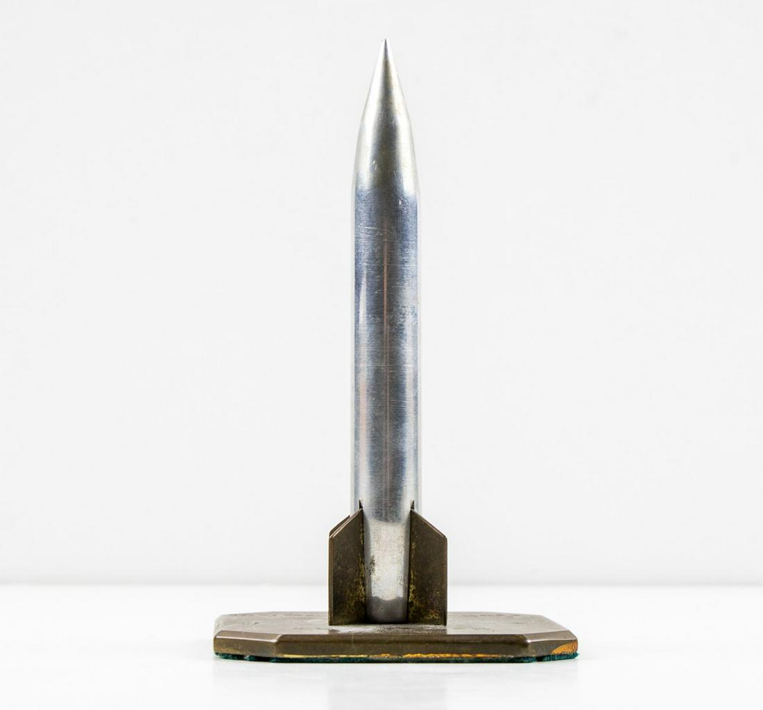 MAJOR GEN. CALEB VANCE HAYNES PRESENTATION CHANUTE: Desktop model of a rocket presented to General Caleb Vance Haynes. The 5.5 in. tall aluminum rocket has brass fins and rests on a bronze base engraved: "Maj. Gen. C. V. Haynes Chanute A.F.B." Very goo