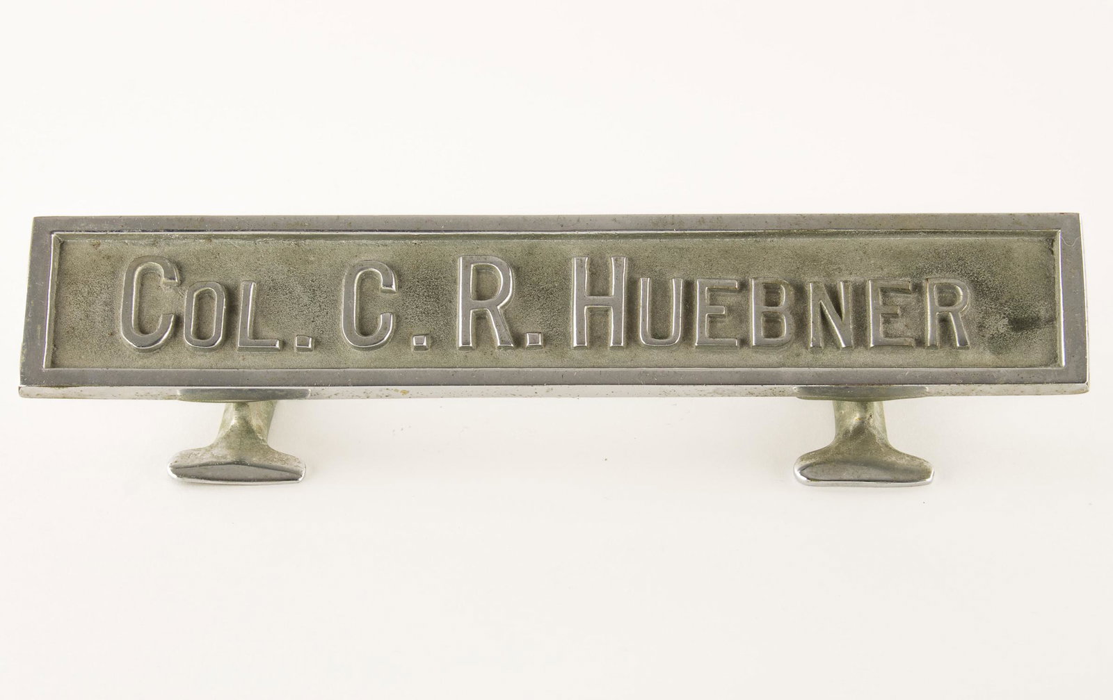 GEN. CLARENCE R. HUEBNER'S WARTIME DESK NAME PLATE: FROM THE ESTATE OF GEN. CLARENCE R. HUEBNER, COMMANDER OF THE 1ST INFANTRY DIVISION IN THE FIRST WAVE AT OMAHA BEACH Solid steel desk nameplate bearing Huebner's name and rank 'Col. C. R. Huebner'. Th