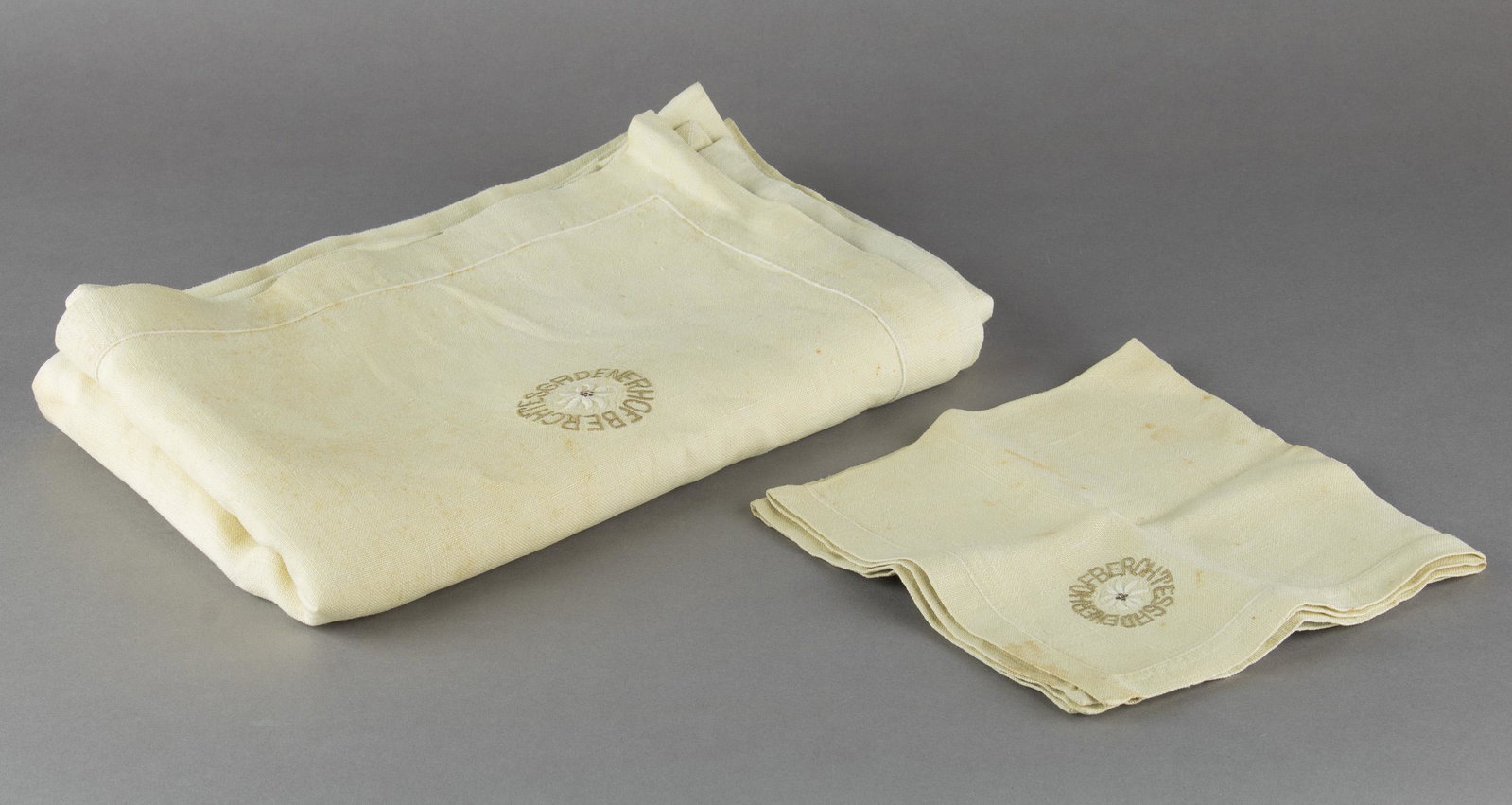 BERCHTESGADENER HOF TABLECLOTH AND NAPKIN: Pair of fine beige linen items from the famous Berchtesgadener Hof, the inn and restaurant located near Hitler's Berghof at Berchtesgaden. Included is a cream white tablecloth, 96 x 62 in., as well as
