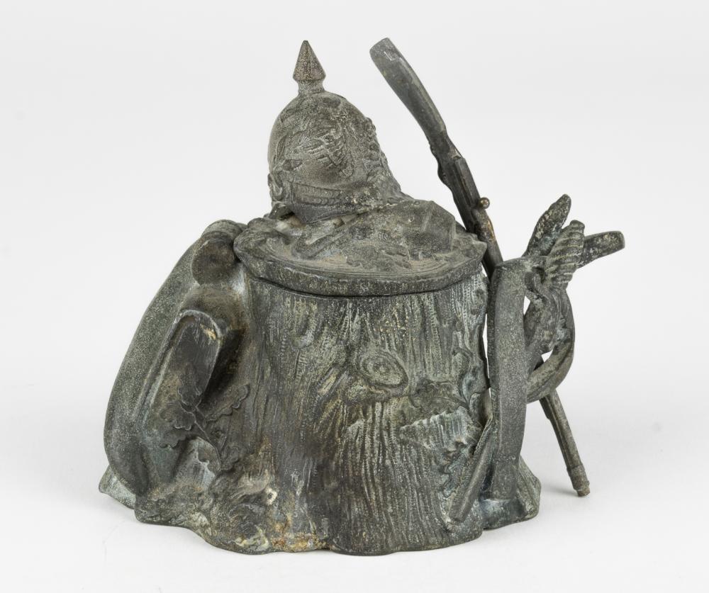 IMPERIAL GERMAN MILITARY-THEMED INKWELL: Imperial-era German inkwell of soft metal alloy, approx. 4 1/4 x 4 1/2 x 3 1/2 in., in the form of a tree stump topped with a soldier's ornamental helmet and canteen, with his pack, bedroll and sword 