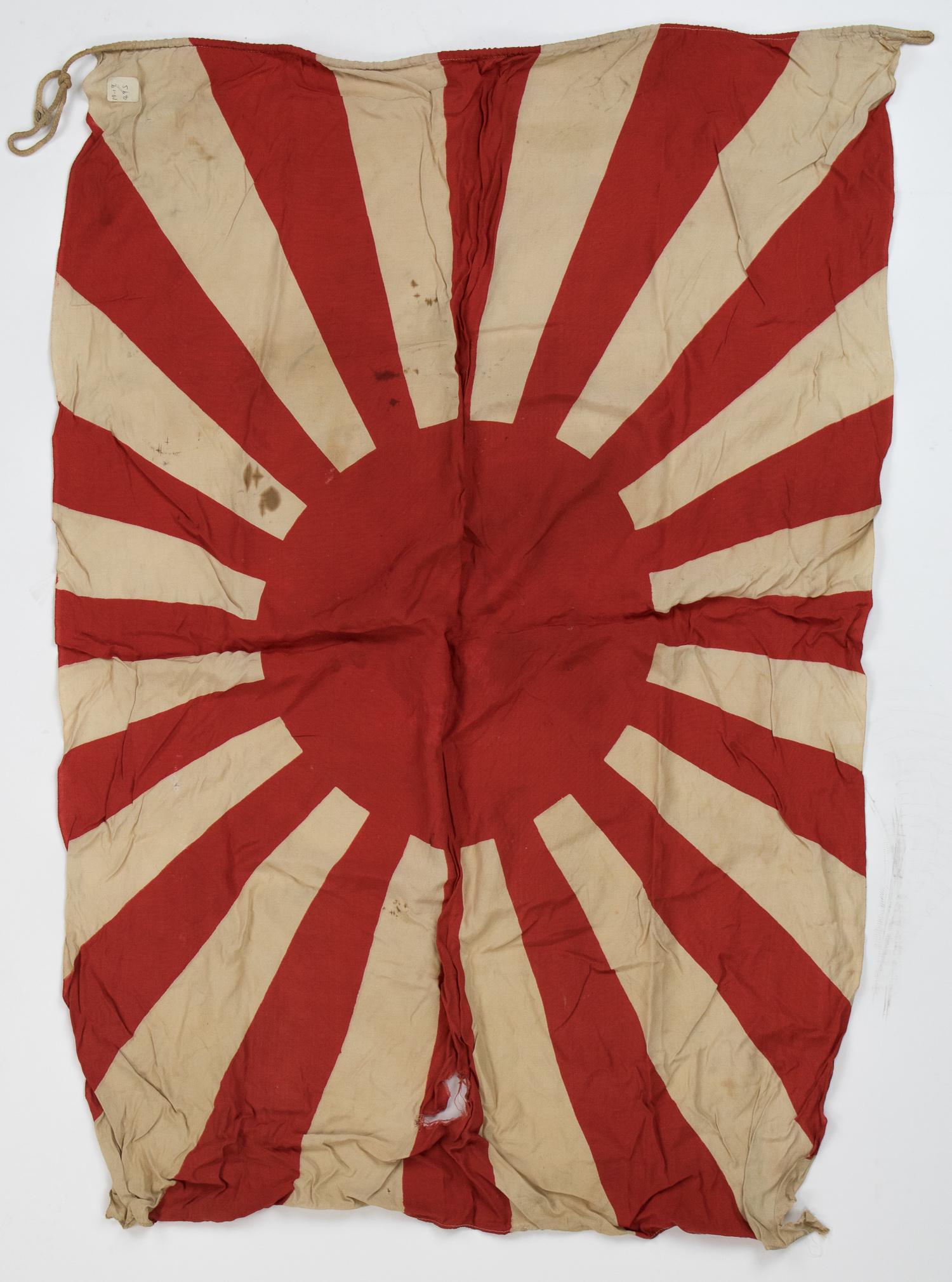 JAPANESE ARMY FLAG: War-period Japanese army flag, 30 x 40 in. cotton construction with a centered 'rising sun' symbol. Cord stitched through the hoist edge, bearing a loop at each end. Scattered stains and tears.
