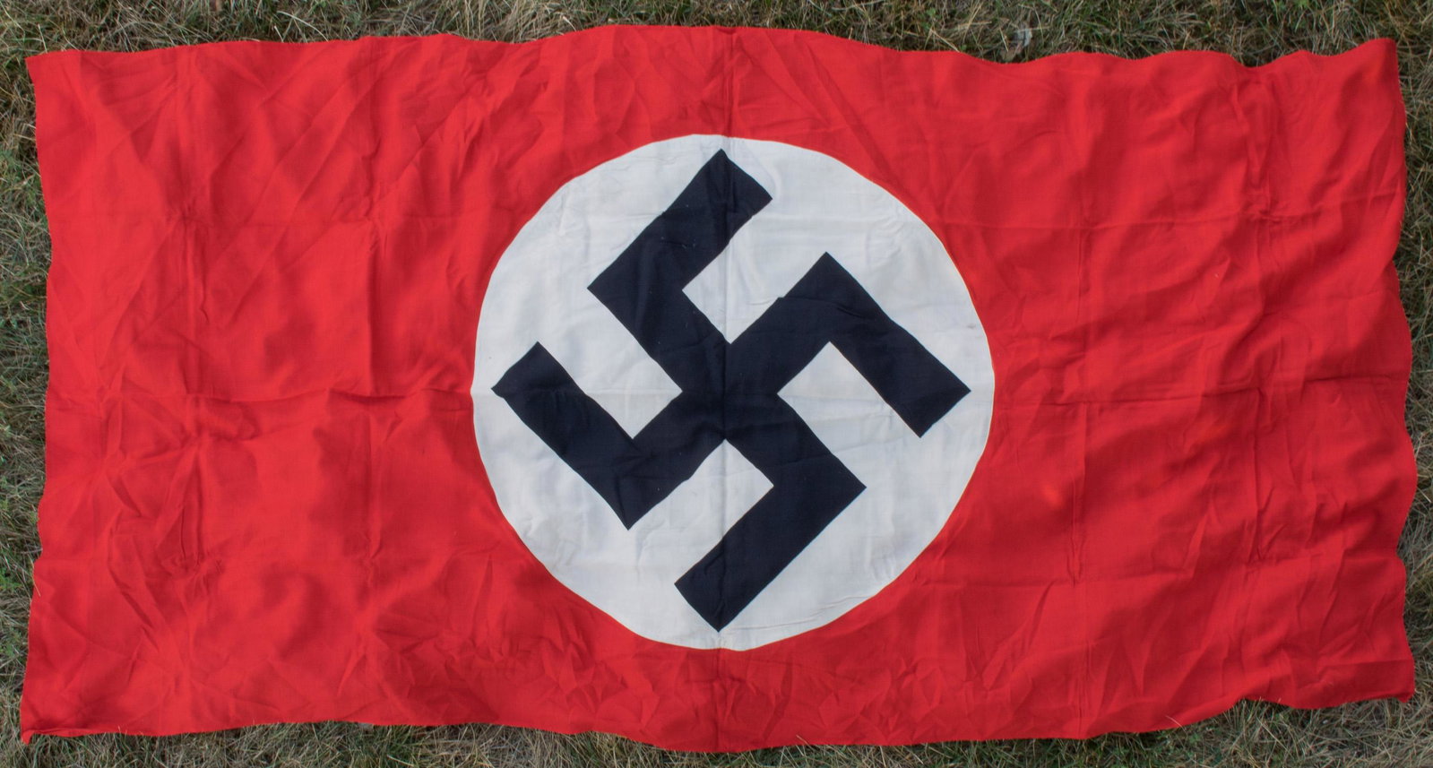 N.S.D.A.P. HANGING BANNER: Large Nazi Party hanging banner, 38 x 76.5 in., constructed of a clamp-dyed mobile swastika on a white disc, then stitched to a red field. The top edge has been folded over and sewn to form a hoist. S