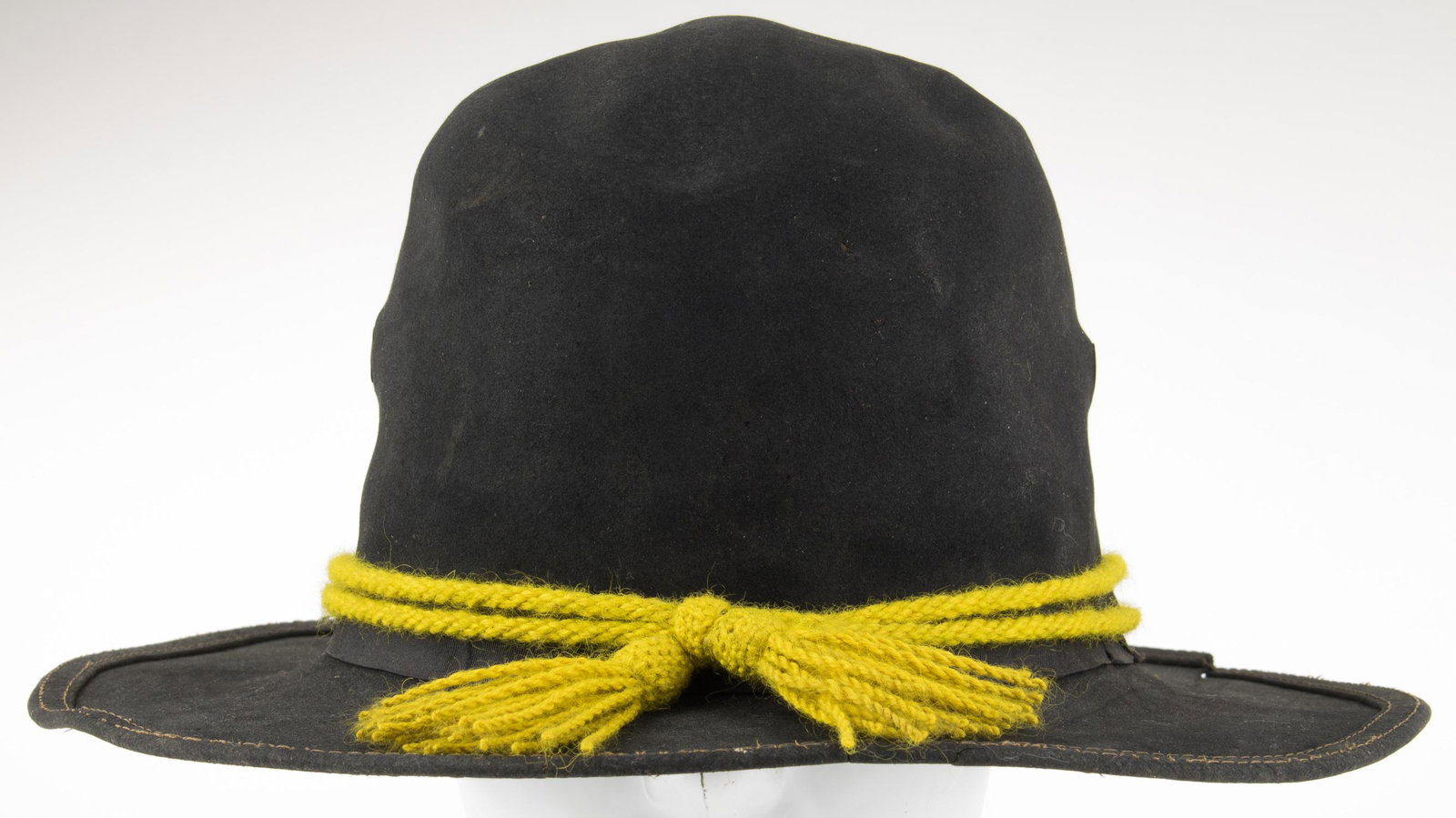 U.S. CAVALRY CAMPAIGN HAT, CA. 1870-1890: Original brown campaign hat once belonging to a U.S. cavalryman, ca. 1870s-1890s, bearing a brown faux leather sweatband, a yellow cap cord and a brass bracher vent on each side. Notable crack to the 