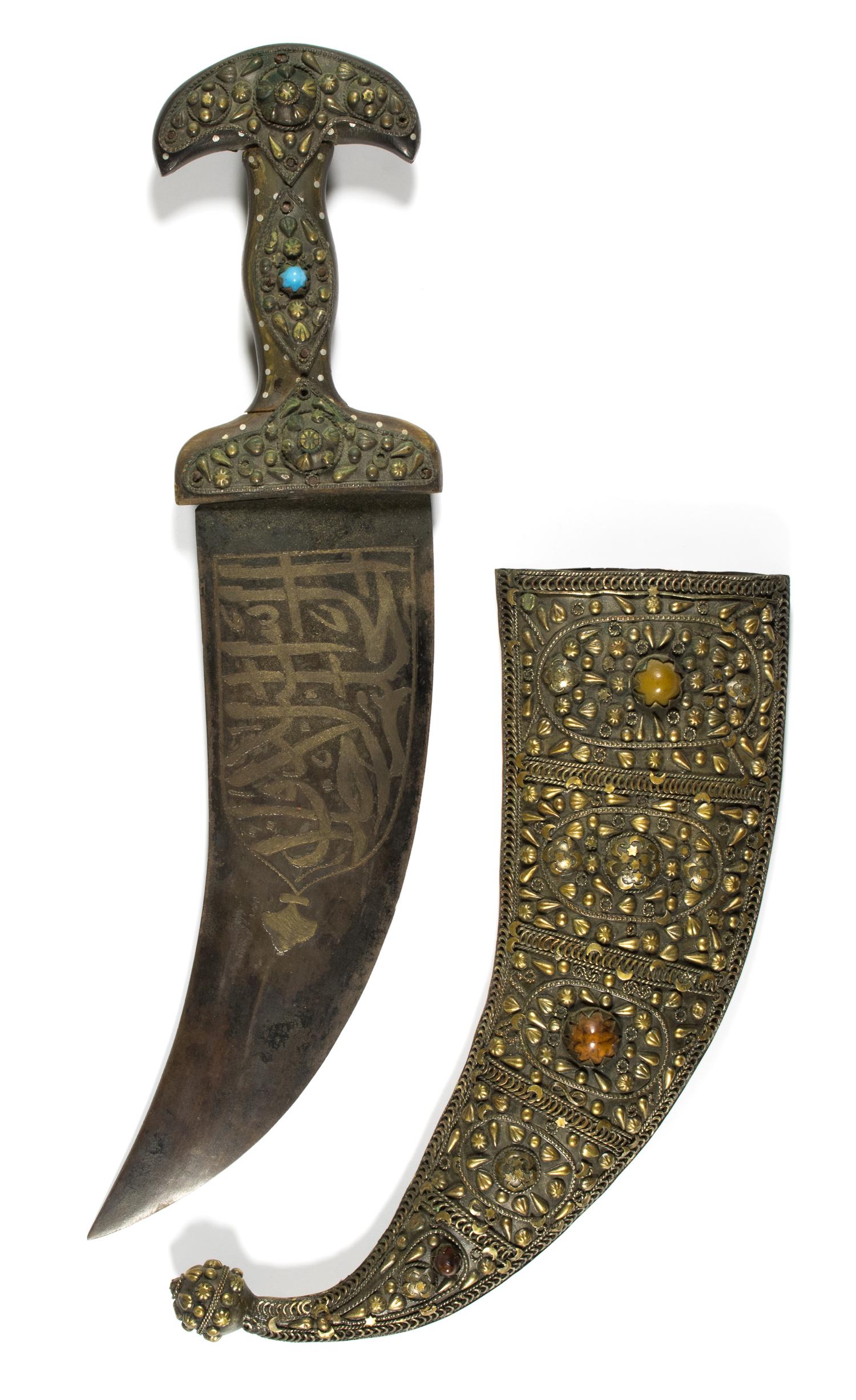 JAMBIYA DAGGER WITH SCABBARD: An Arabian 'Jambiya' style dagger with an intricate brass scabbard, 11.5 in. blade, 17.5 in. overall, encrusted cross guard, pommel, and hilt, the wide blade decorated with Arabic lettering. Curved sc