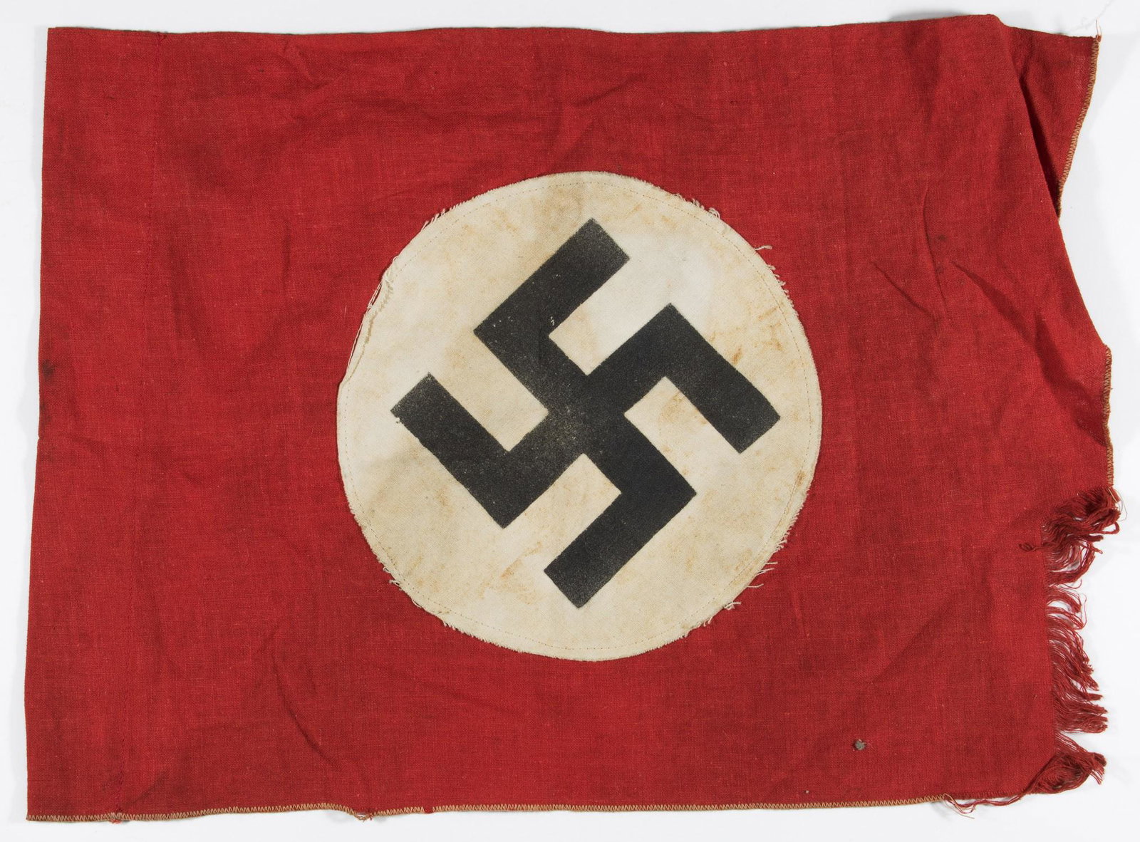 NSDAP FLAG: A small double sided cotton NSDAP flag, 15 x 11 in., red with a sewn white disk bearing a clamp dyed swastika. Folded over and sewn on one side to allow insertion of a suspension rod. Moderate stains,