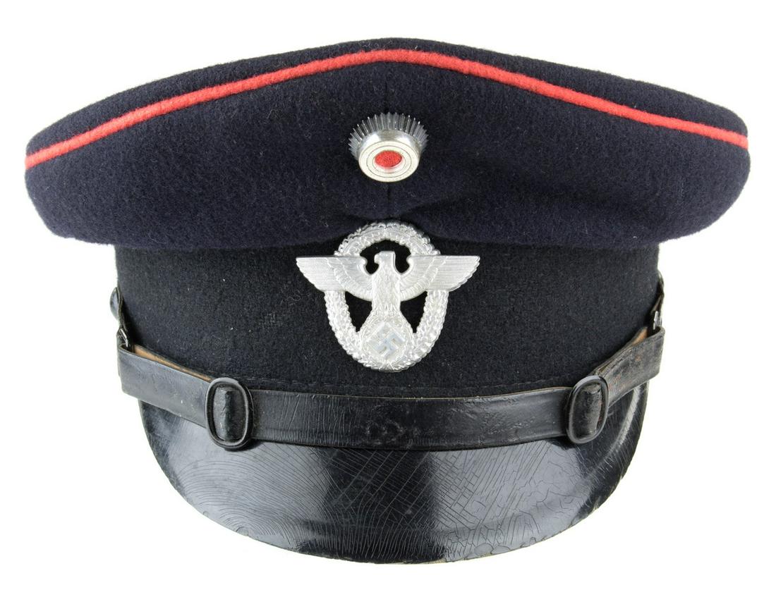GERMAN FIRE POLICE VISOR CAP: German Fire Police visor cap, navy blue wool body with black side band and red piping, bears an aluminum cockade with national eagle and swastika insignia beneath. Leather chin strap is affixed with r