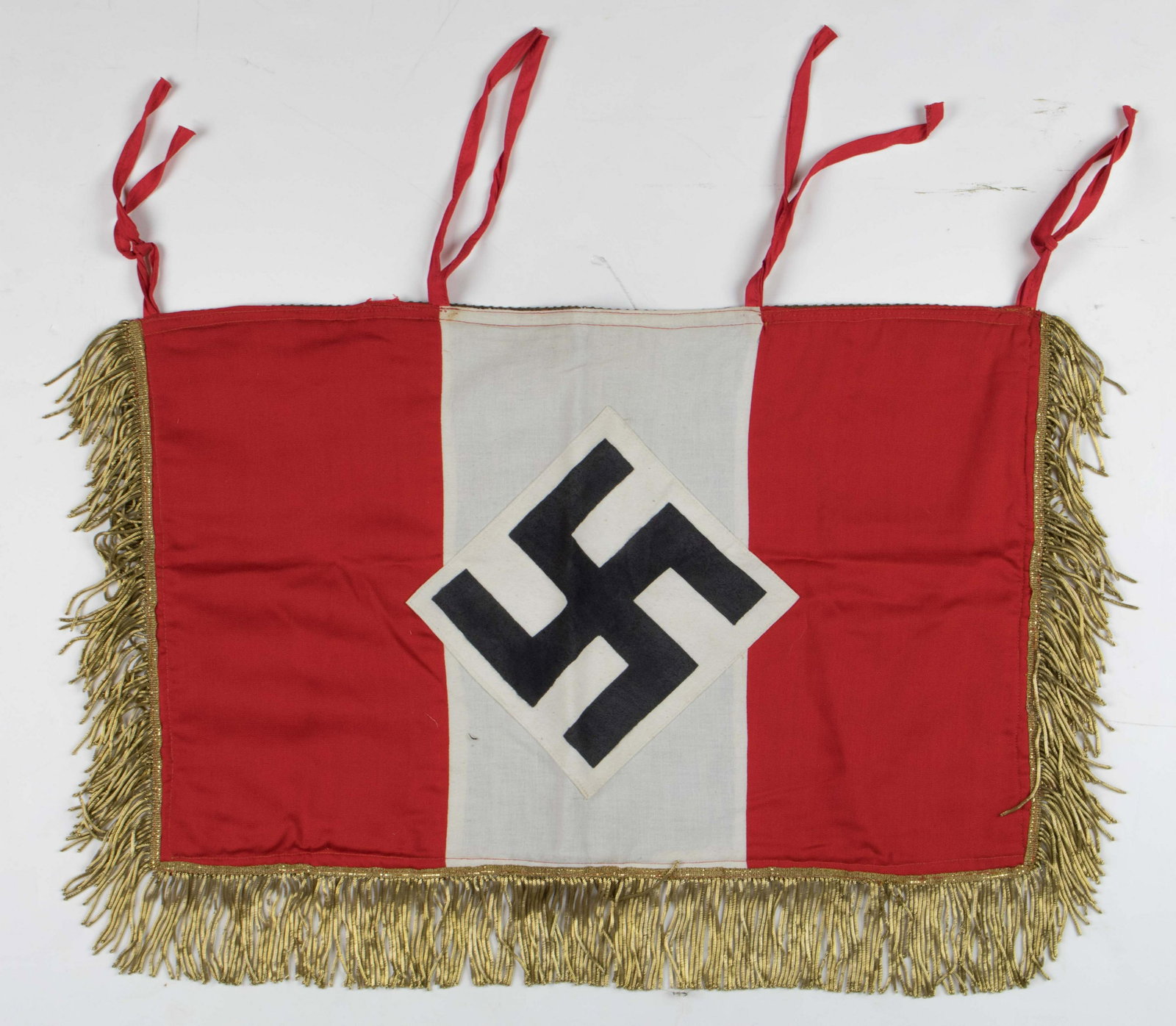 HITLER YOUTH DRUM BANNER: A scarce one-sided Hitler Youth drum banner, approx. 24.5 x 14.5 in., properly constructed in red and white sections with sewn swastika at the center, stitched with a gilded border and 3 in. gold tass