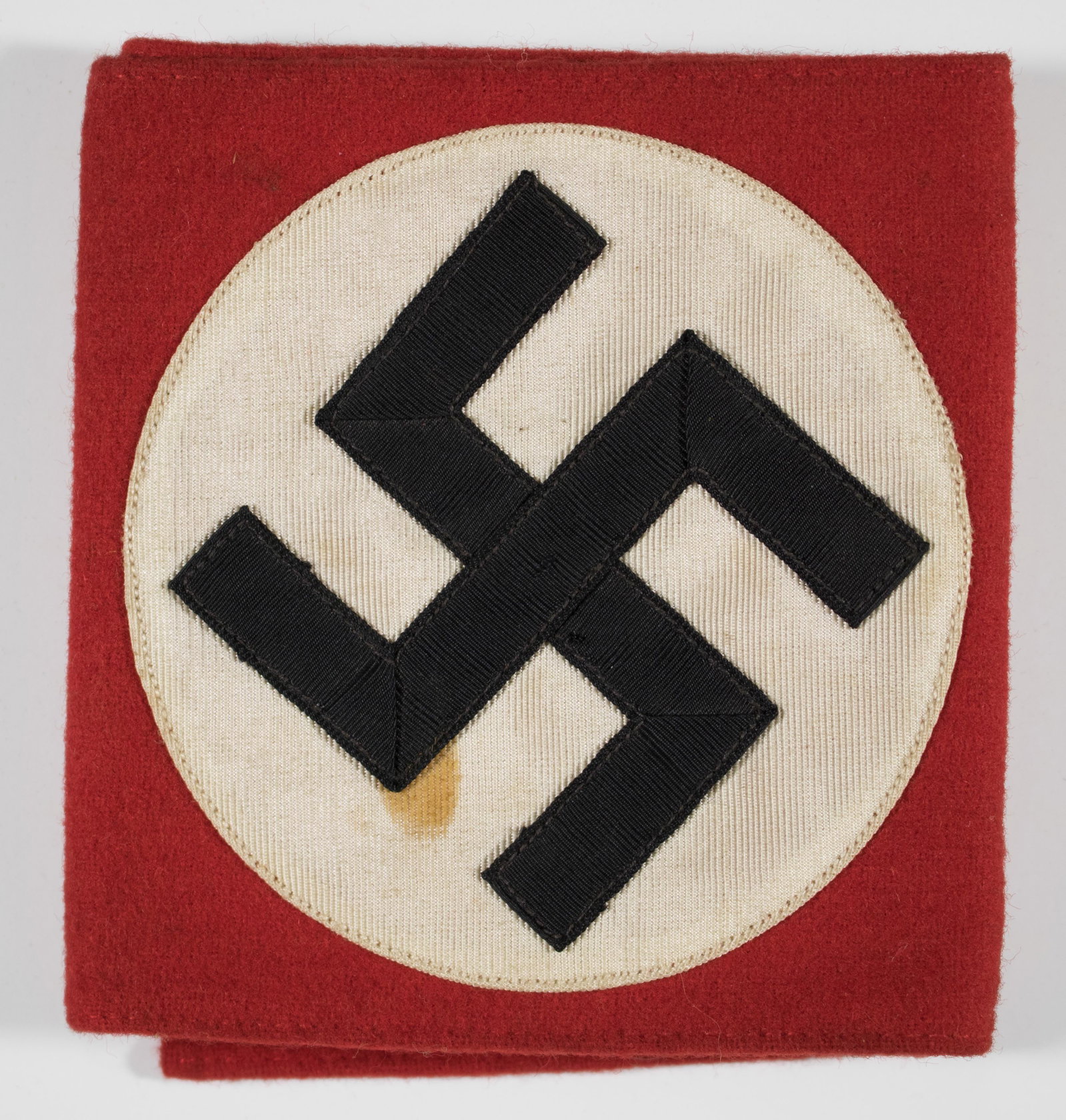 N.S.D.A.P. ARMBAND: NSDAP armband, heavy wool three-piece construction 19 x 4.5 in., separate white field and ribbon-type swastika sewn to the red backing. Paper RZM tag affixed to the reverse. Several minor moth holes, 
