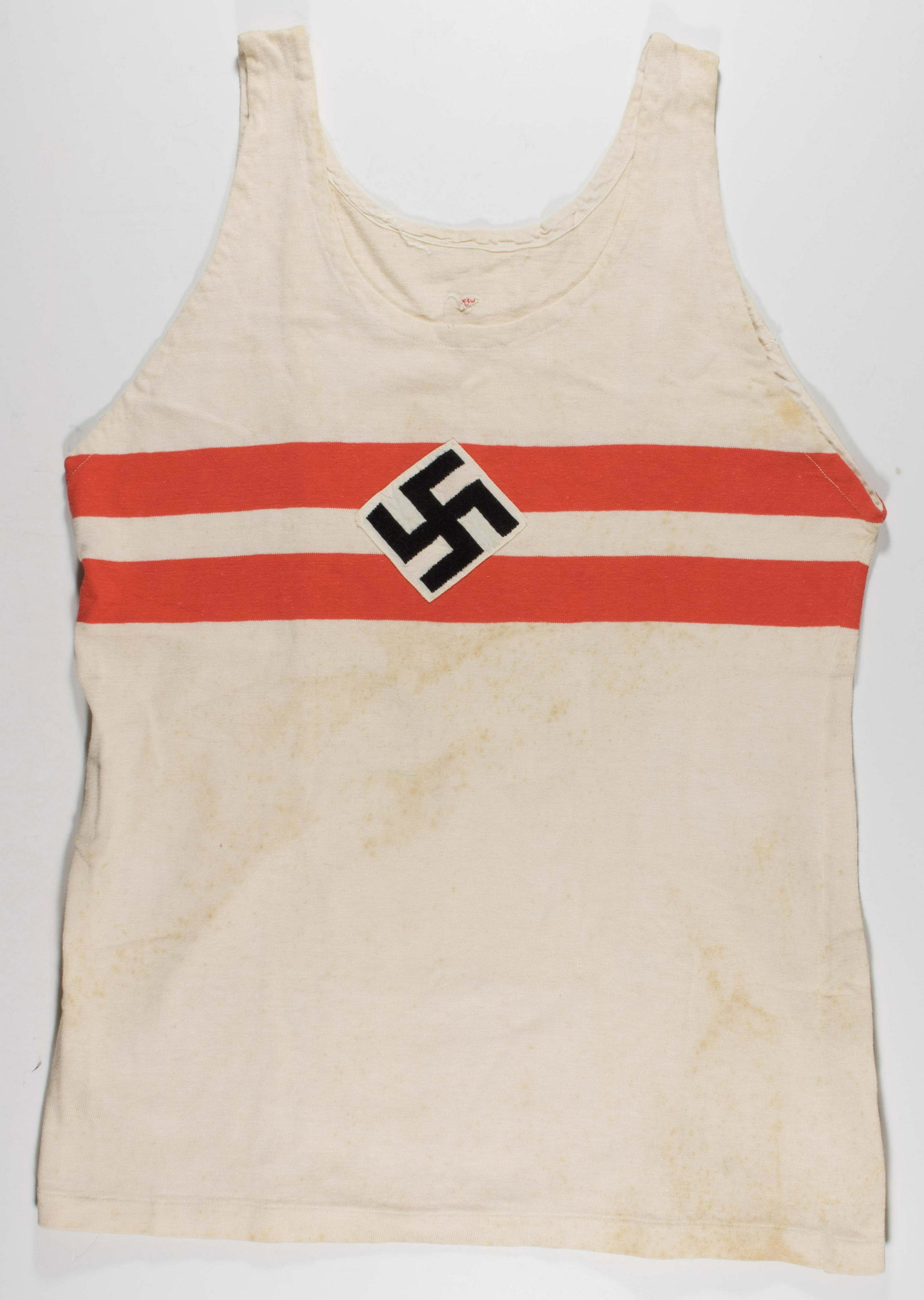 HITLER YOUTH SPORT SHIRT: White cotton sleeveless Hitler Youth athletic shirt, 23 in. shoulder to hem, with a printed red-and-white band and an applied cloth Hitler Youth mobile swastika in the center of the chest. Moderately 