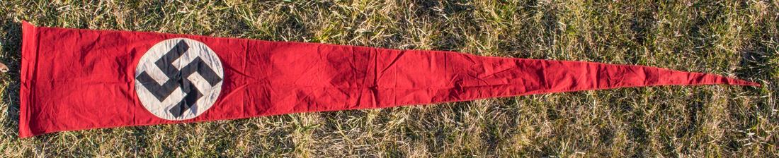 LARGE NSDAP PENNANT: Lengthy two-sided cotton triangular NSDAP pennant, roughly 17 x 106 in., white disk swastika stitched to the center, left side folded and sewn to form a pipe pocket. Lightly worn, with stains and a fe