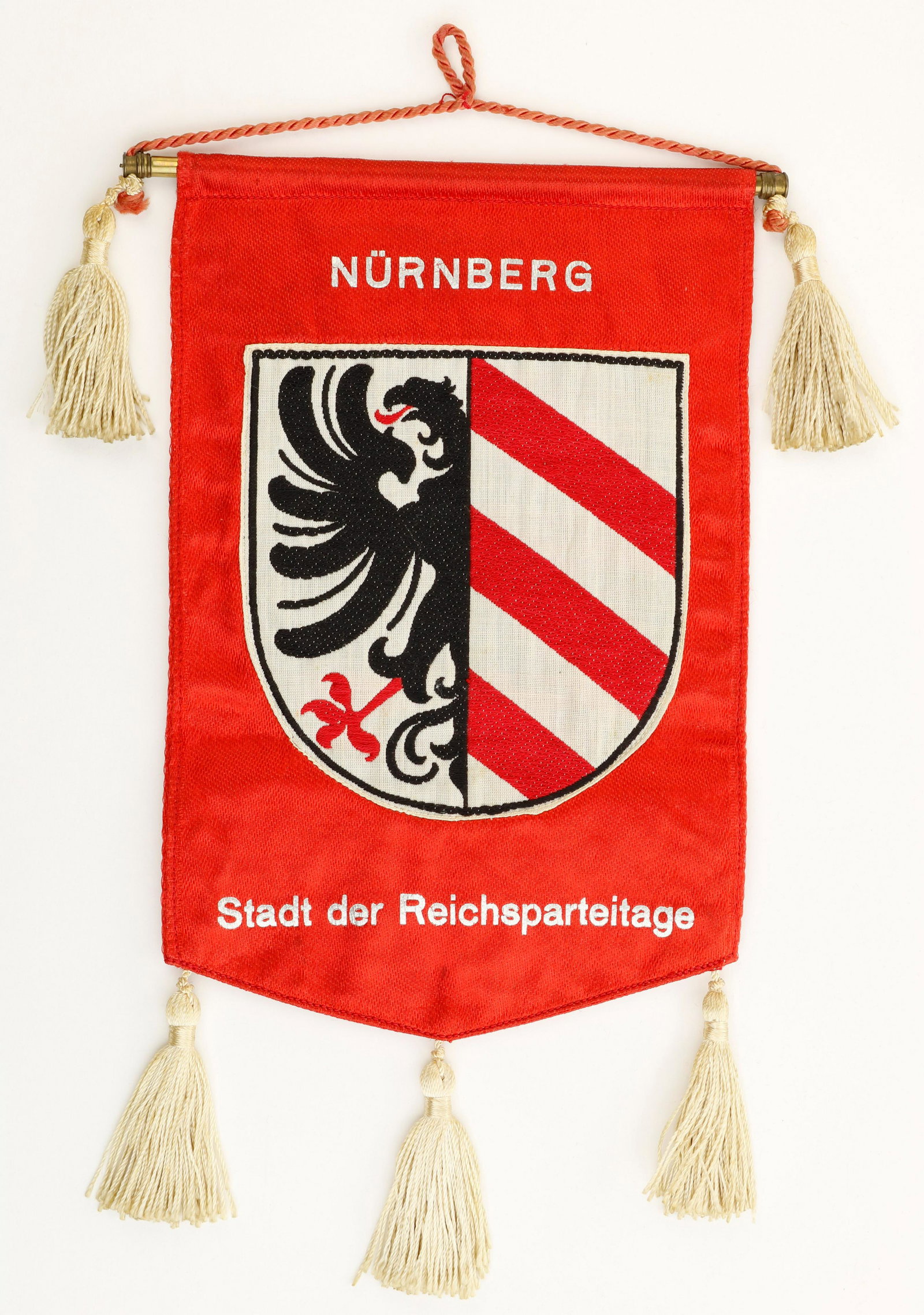 NUREMBERG REICHS PARTY DAY TABLE FLAG: Nuremberg Reichs Party Day Flag, 5 x 7.75 in. rayon with five decorative beige tassels and red cord for suspension. The flag bears a BeVo. swastika applied to the red rayon body on one side, the rever