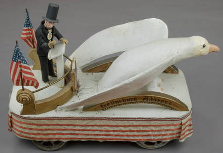 ABRAHAM LINCOLN TOY PARADE FLOAT: A patriotic float pull toy, 24 in. long, 11. in. across and standing 17.5 in. tall, consisting of a wooden base with a metal covering wrapped around the side with four wheels attached to allow for