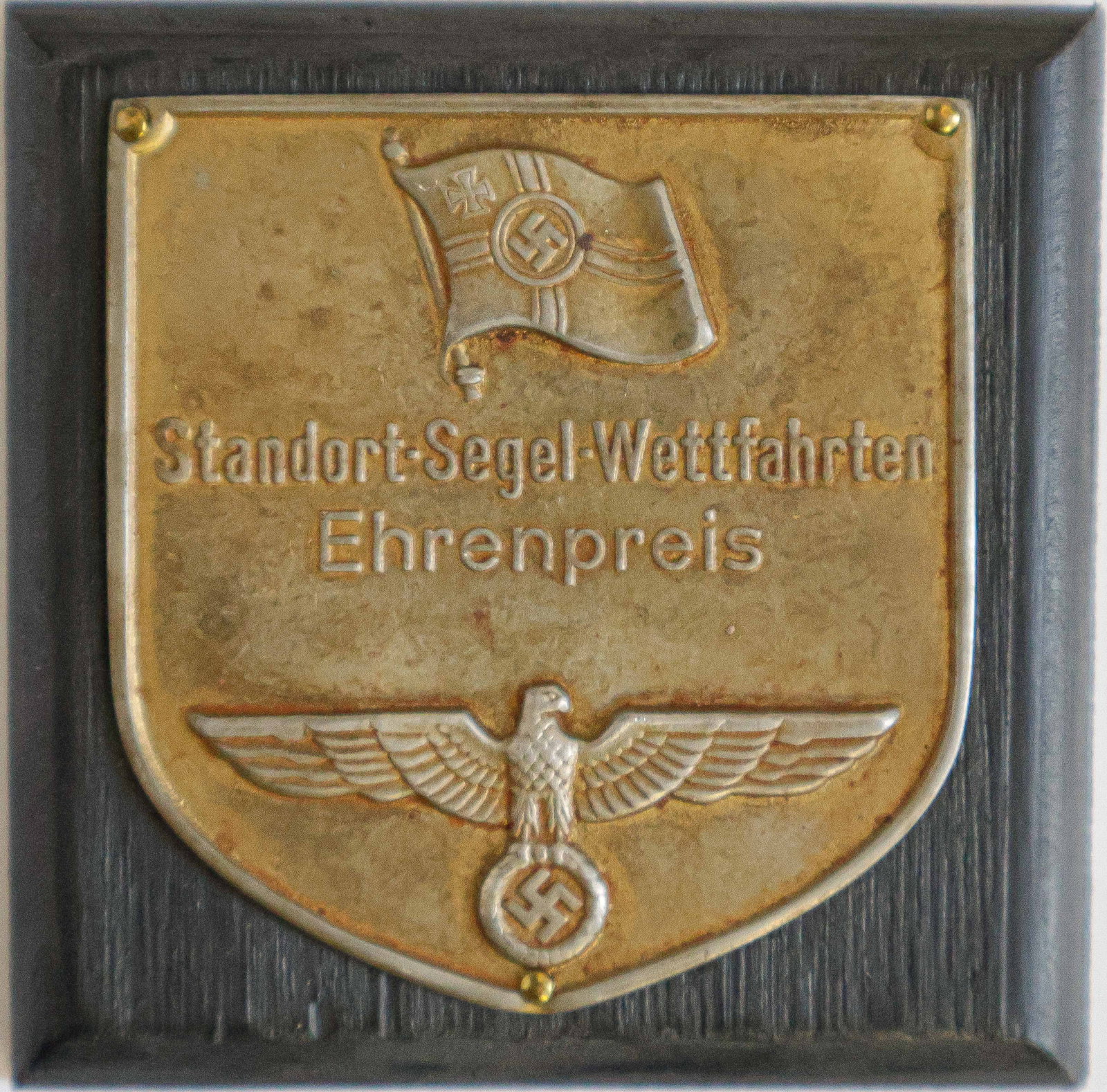 KRIEGSMARINE EHRENPREIS PLAQUE: Bronze award plaque, 2.5 in. dia., depicting the Reiches Kriegs Flagge and the German national eagle with swastika and wreath. The text between both images reads: ‘Standort Segel Wettfahrten Ehr