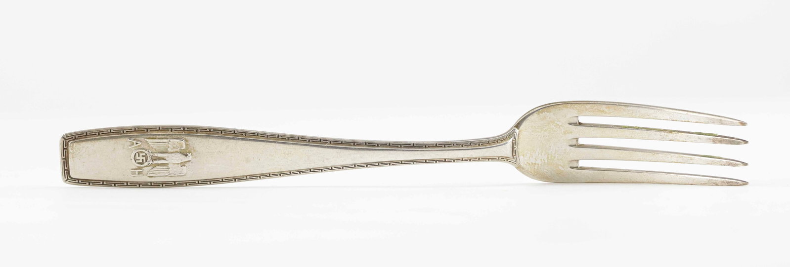 ADOLF HITLER FORMAL APPETIZER FORK: Delicate sterling silver four-tined formal appetizer fork from the personal set of Adolf Hitler's table silverware, 5.75 in. long. The otherwise simple and unadorned handle terminates with a national 