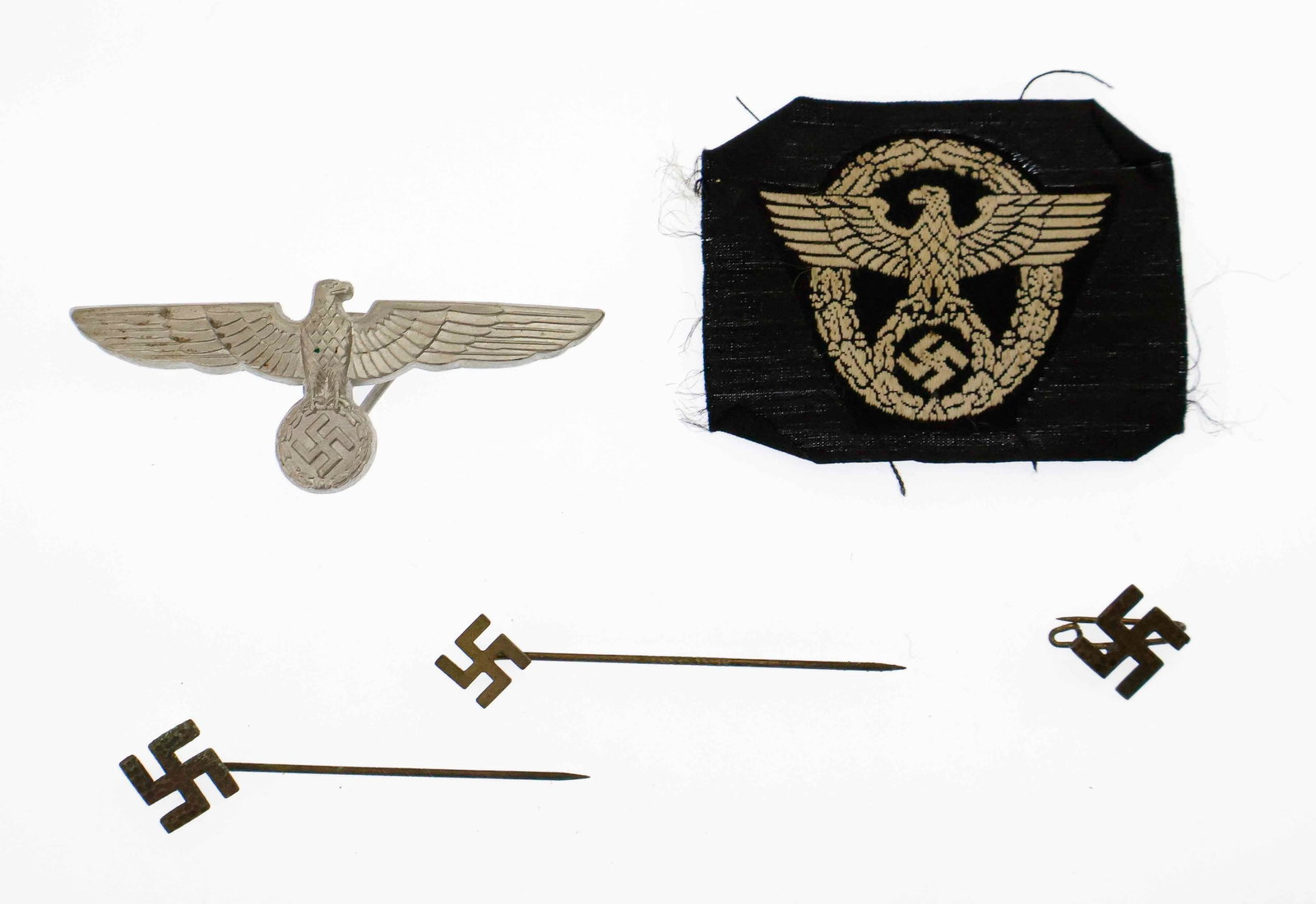 GERMAN INSIGNIA GROUPING (5): Grouping of five various metal and cloth German insignia, includes: SS police BeVo embroidered cap eagle, aluminum cap eagle, and three swastika stickpins. Very good.