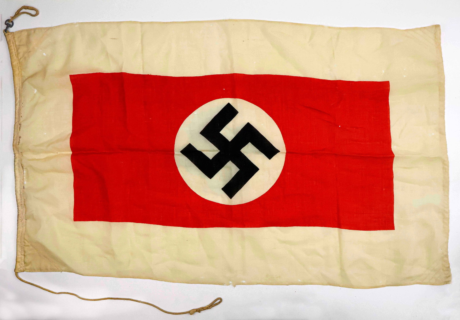 THIRD REICH HARBOR PILOT FLAG: Rare flag, 26 x 46 in., a printed NSDAP national flag with a white border. The flag features a sewn-in rope hoist, with a metal hanging device at one end and loose lanyard on the bottom. In fair state