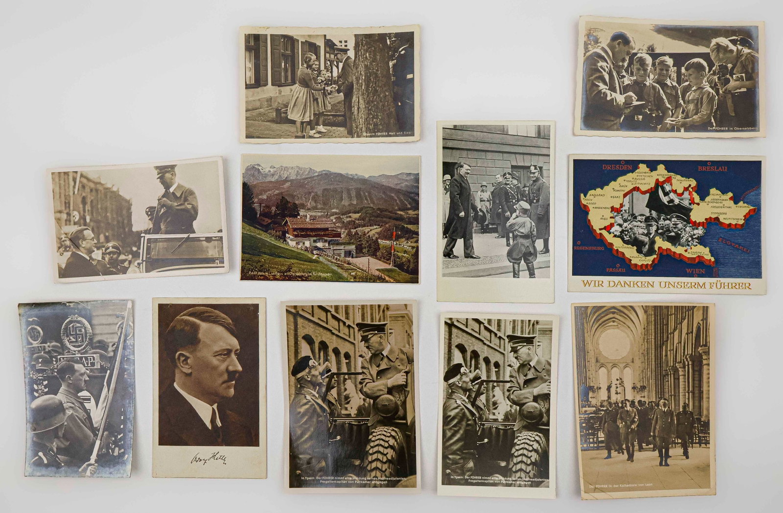 ADOLF HITLER POSTCARD COLLECTION (11): A fine group of 11 original postcards showing Adolf Hitler in various scenarios such as marching in a parade, signing autographs for Hitler Youth, greeting German girls who offer him flowers, in Ypres