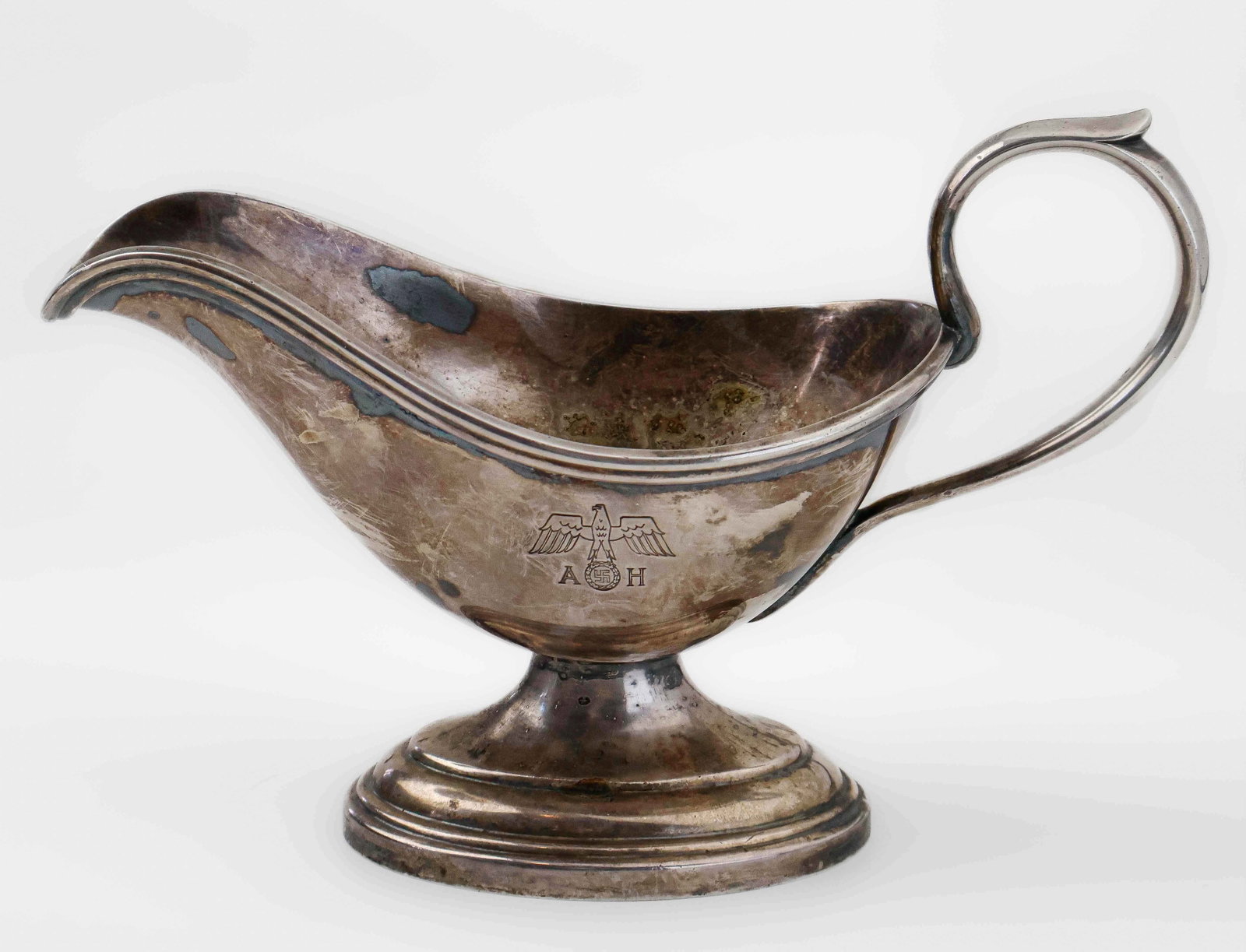 ADOLF HITLER GRAVY BOAT: An excessively rare silver gravy boat from Adolf Hitler’s formal service set, 10 x 6.5 in., featuring a national eagle and swastika flanked by the initials 'A' and 'H'. The tray to which this gr